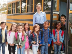Elementary,School,Teacher,And,Pupils,Standing,By,School,Bus
